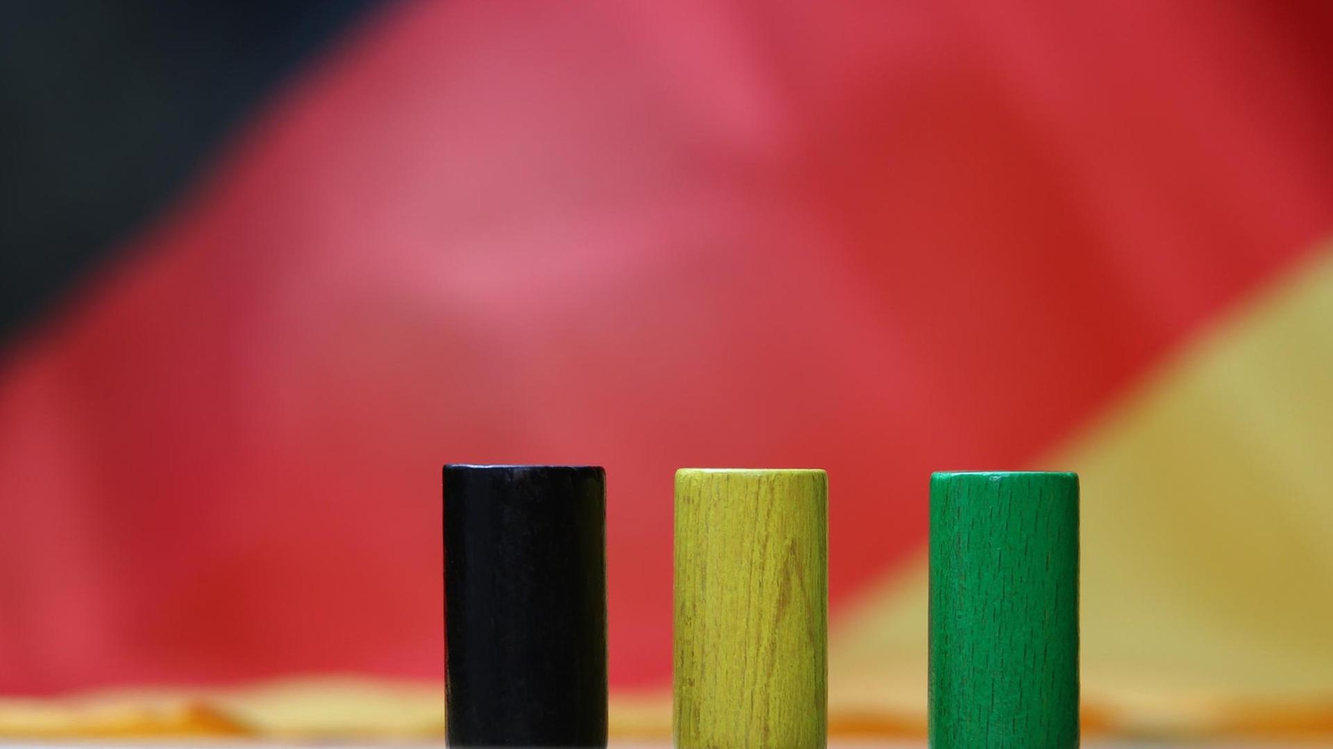 Drei hölzerne Spielsteine in den Farben Schwarz, Gelb und Grün stehen auf einer Deutschlandfahne.