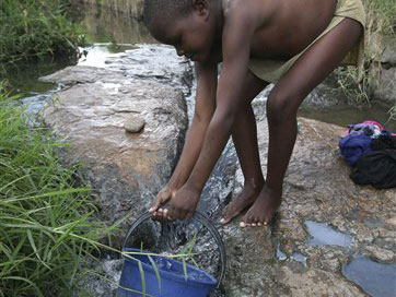 Ein Junge schöpft Wasser aus einem Fluss in Harare, Simbabwe.