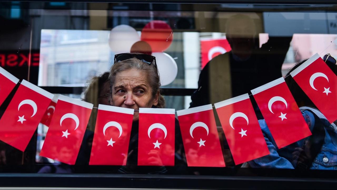 Eine Frau in Istanbul schaut aus einem mit türkischen Fahnen geschmückten Fenster