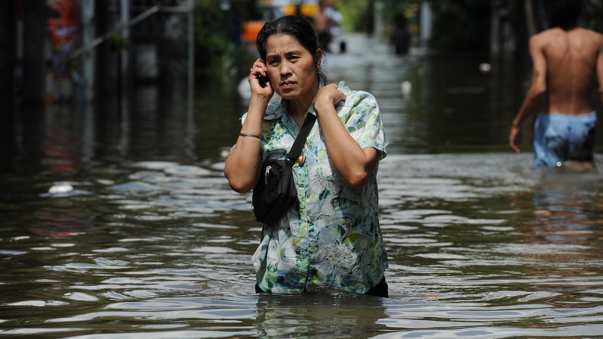 Eine Frau steht hüfthoch im Hochwasser und telefoniert per Handy