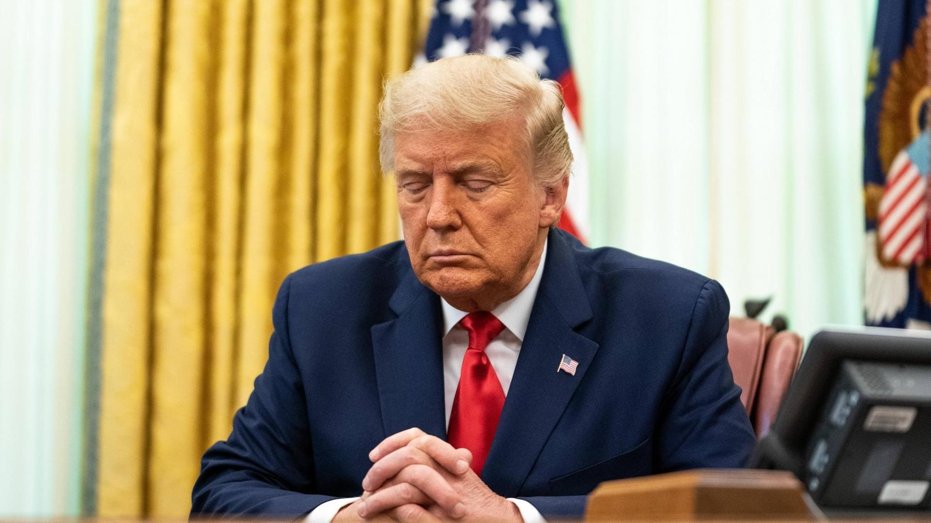 US-Präsident Donald Trump sitzt mit geschlossenen Augen und gefalteten Händen beim Beten im Oval Office an seinem Schreibtisch, nachdem er eine Strafgefangene von ihrer lebenslangen Haftstrafe begnadigt hat.