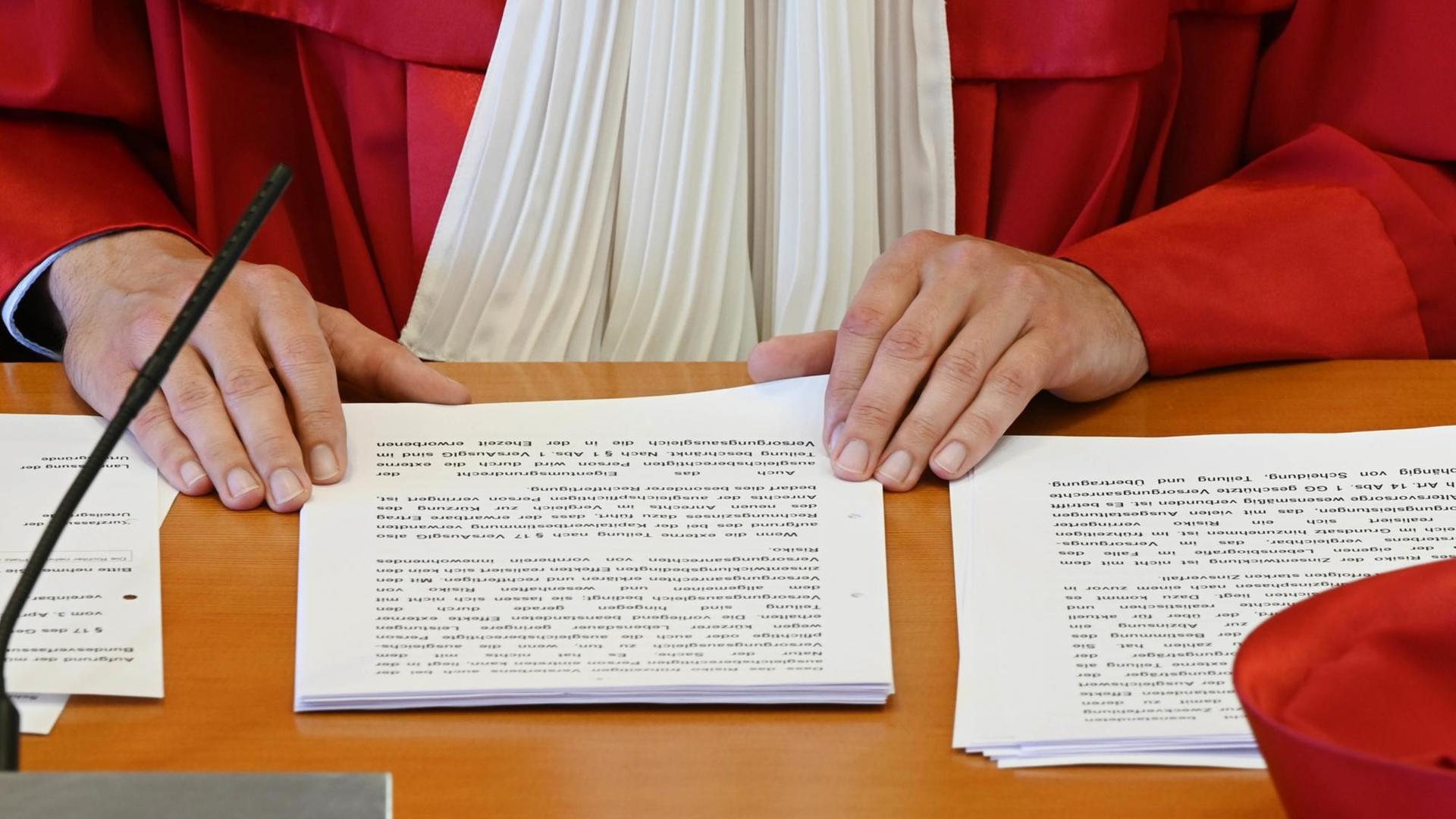 Die Hände eines Richter in roter Robe des Bundesverfassungsgerichts und das Urteil auf dem Tisch