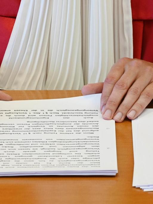 Die Hände eines Richter in roter Robe des Bundesverfassungsgerichts und das Urteil auf dem Tisch