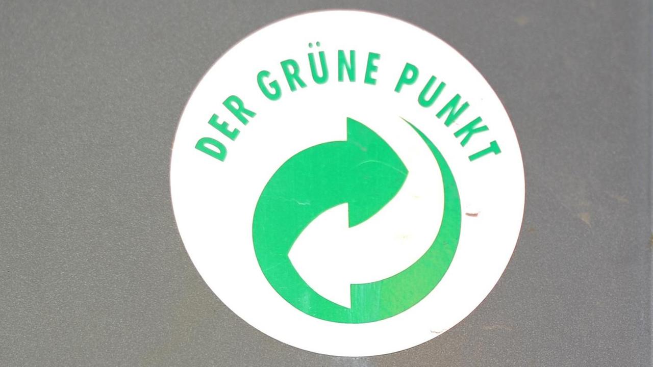 Ein Aufkleber mit dem Logo "Der Grüne Punkt" klebt auf einem Mülleimer.


