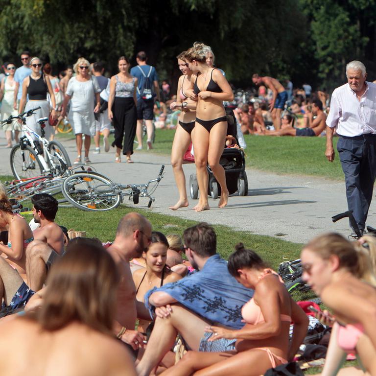 Großer Besucherandrang an Sonnenhungrigen und Spaziergängern sowie Touristen am Eisbach im Englischen Garten an einem heißen Sommertag in München.