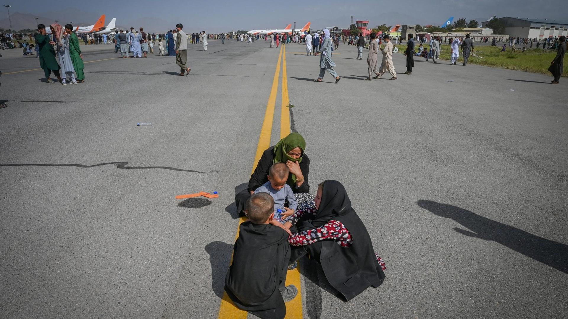 Afghanistan, Kabul: Menschen sitzen auf dem Rollfeld des Flughafens.