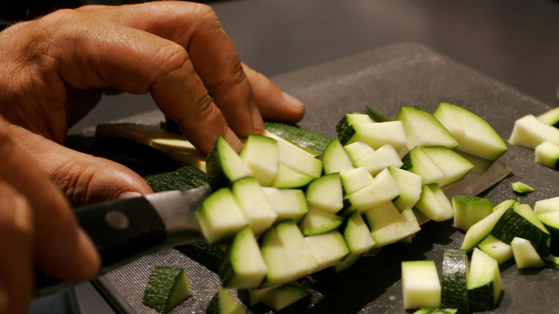 Zucchini wird auf einem Brettchen in kleine Würfel geschnitten,