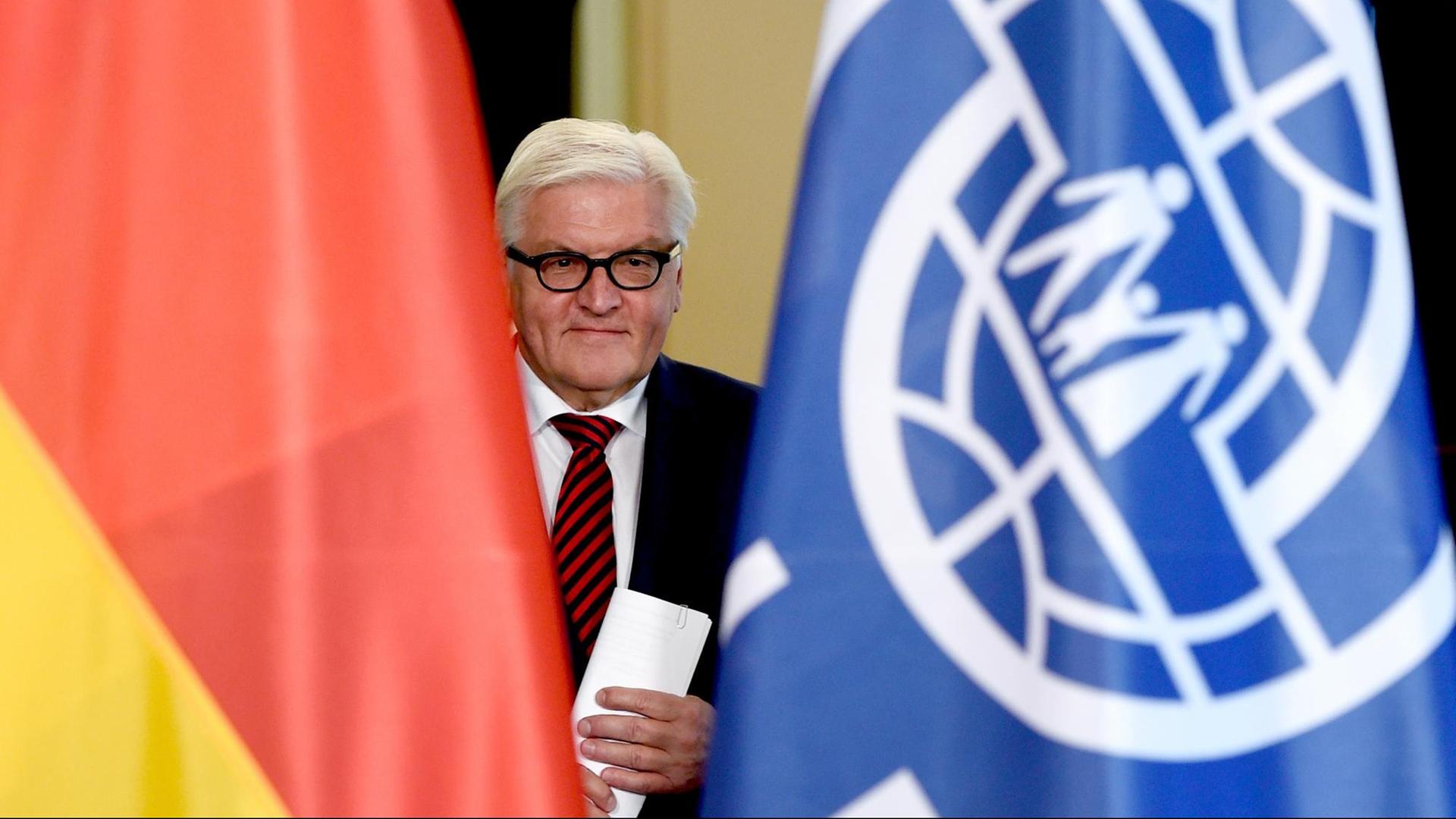 Frank-Walter Steinmeier zwischen zwei Flaggen der Bundesrepublik Deutschland und der Internationalen Organisation für Migration