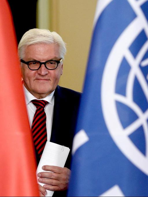 Frank-Walter Steinmeier zwischen zwei Flaggen der Bundesrepublik Deutschland und der Internationalen Organisation für Migration