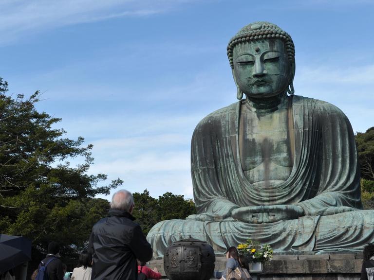 Touristen beobachten eine Buddha-Statue am Kotoku-in Tempel in Kamakura, Präfektur Kanagawa im Osten Japans. Die 11,5m hohe Bronze Statue wurde im Jahr 1252 konstruiert und ist die zweitgrößte Buddha Statue in Japan nach dem großen Buddha in Nara.
