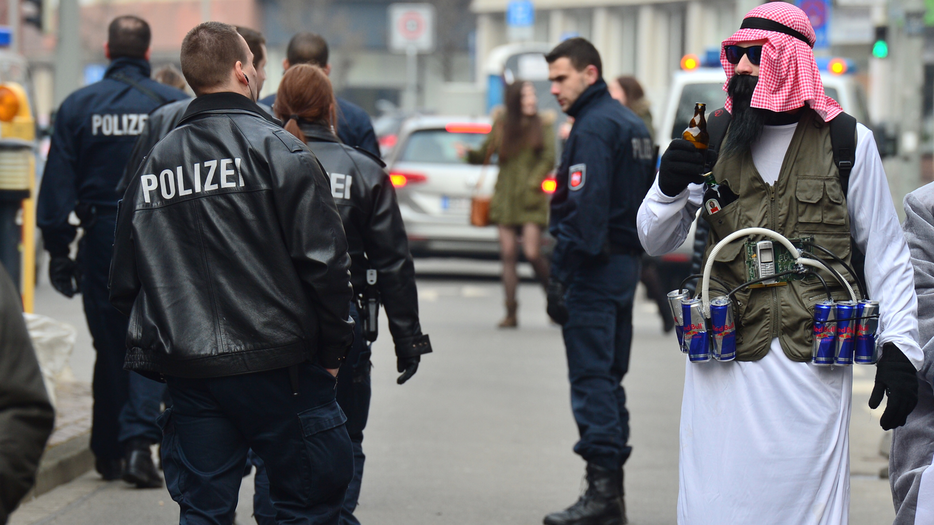 Karnevalist Sebastian (23), verkleidet als Terrorist mit "Sprengstoffgürtel" aus Energy-Drinks, steht am 15.02.2015 neben Polizisten in Braunschweig (Niedersachsen)
