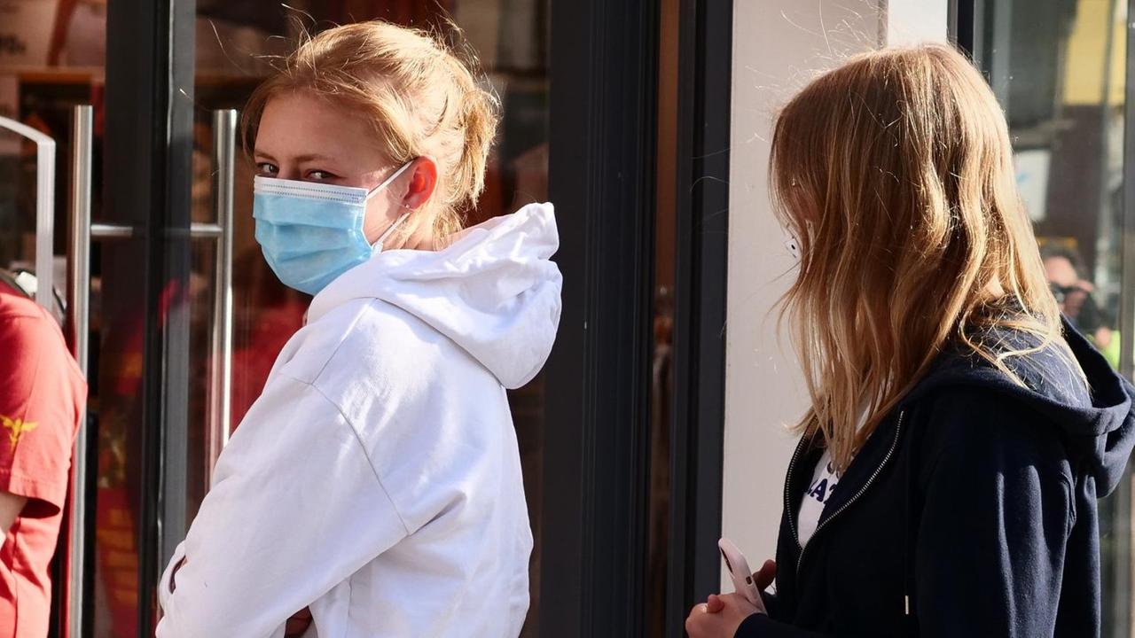 Zwei junge Frauen stehen in Berlin vor einem Bekleidungsgeschaeft Schlange mit Abstand zueinander und mit Masken gegen das neuartige Coronavirus.