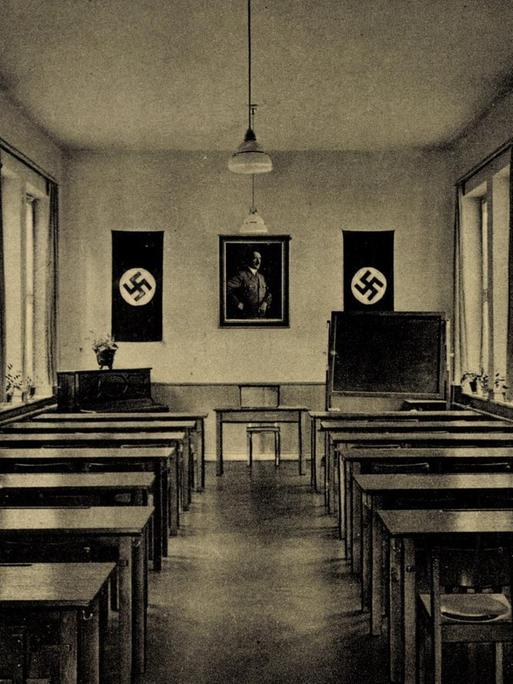 Eine Schwarzweißpostkarte zeigt in Zentralperspektive einen langgestreckten Sitzungssaal mit Reihen von Pulten jeweils an der rechten und der linken Seite des Raumes. Am Kopfende sind zwei Hakenkreuze und ein Führerbild, das Adolf Hitler abbildet, zu sehen.