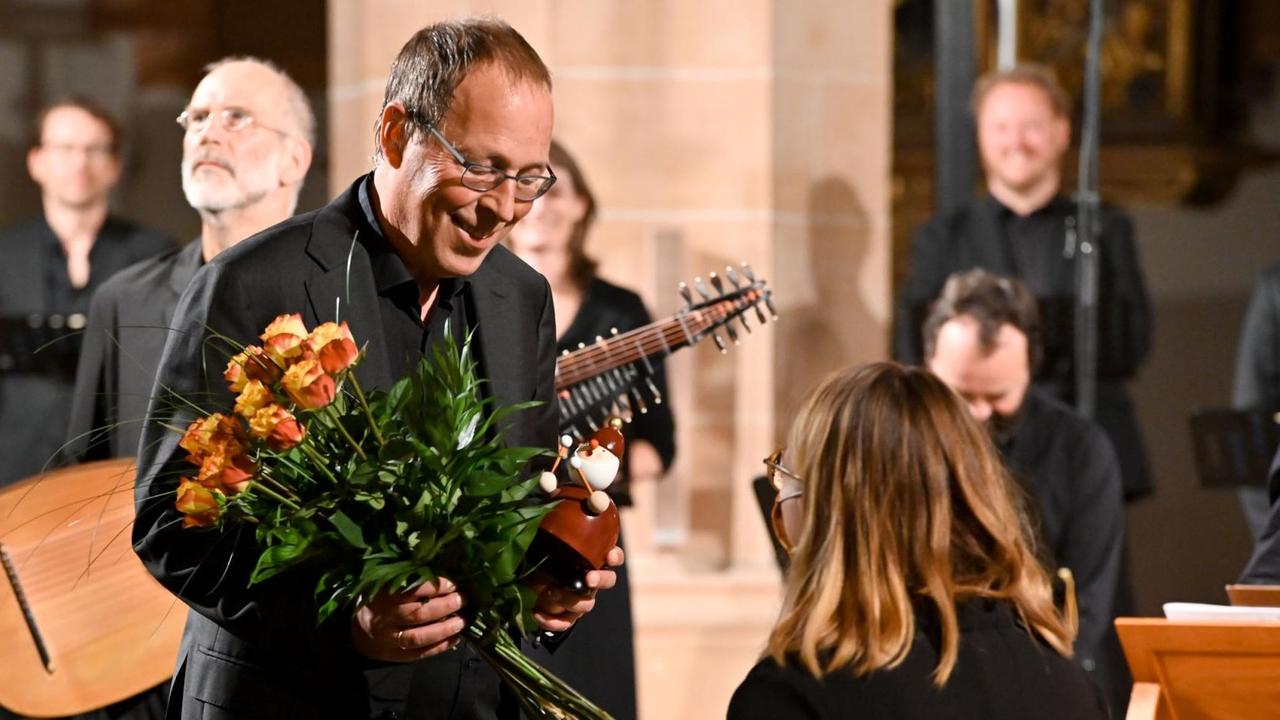Ein Dirigent erhält einen Straus mit gelben Rosen und einen Räuchemann, der Paukenschlegel in der Hand hält.