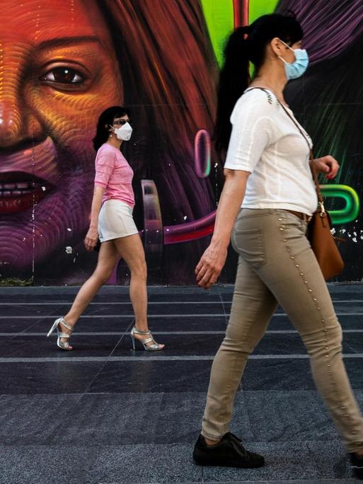 Drei Frauen gehen mit großem Abstand zueinander an einem bunten Graffito in Madrid vorbei.