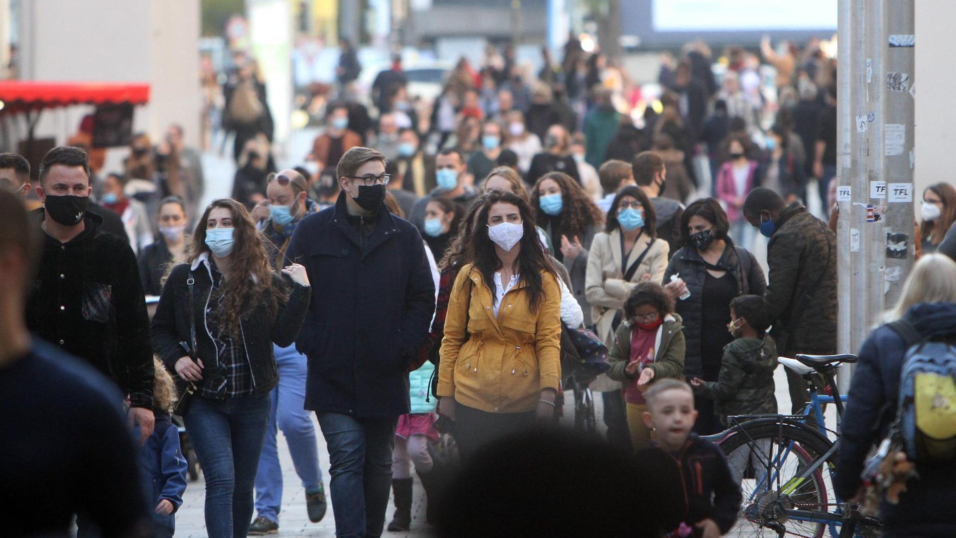 Menschen mit Masken laufen durch die Fußgängerzone Neuhauser Straße am Karlstor in der Innenstadt von München.