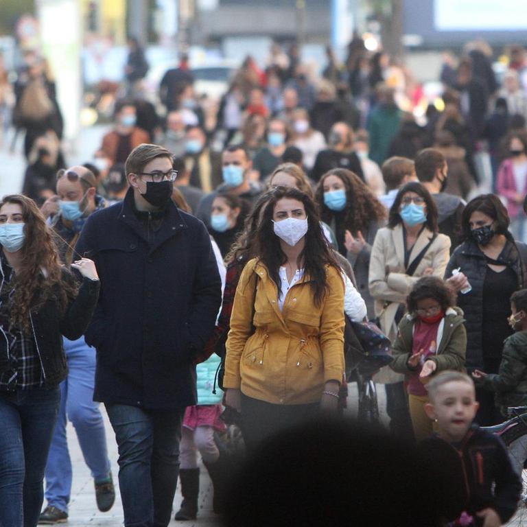 Menschen mit Masken laufen durch die Fußgängerzone Neuhauser Straße am Karlstor in der Innenstadt von München.