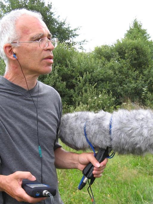 Peter Cusack mit Aufnahmegerät und großem Windschutz bei Feldaufnahmen in offener Landschaft