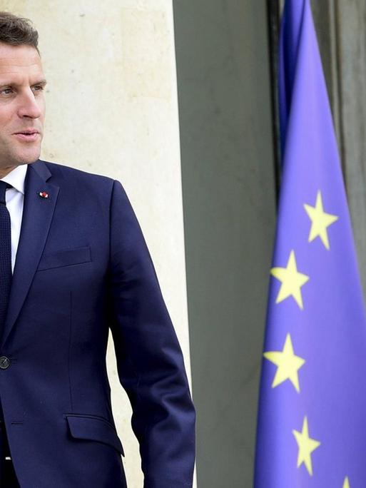 Macron steht vor einer französischen und einer EU-Flagge.