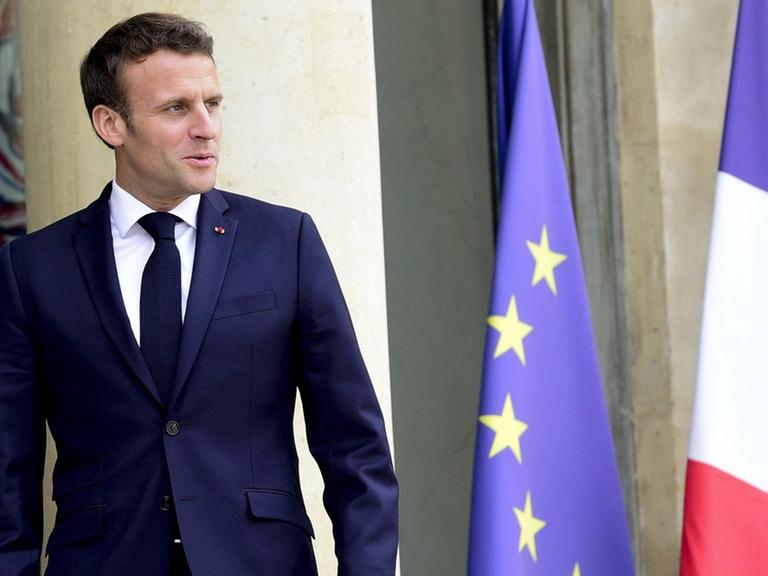 Macron steht vor einer französischen und einer EU-Flagge.