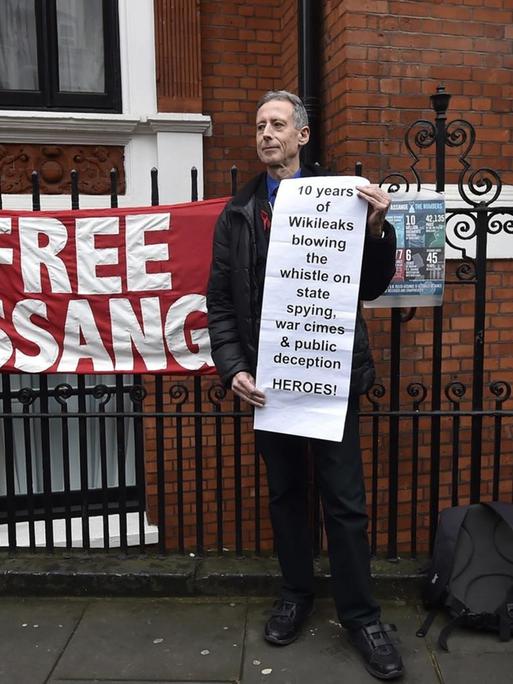 Der Mann steht vor dem Zaun der Botschaft und trägt ein Transparent, auf dem Wikileaks als "Heroes" bezeichnet wird. Ein Polizist läuft an ihm vorbei. Am Zaun hänge Transparente, eines mit der Aufschrift "Free Assange".