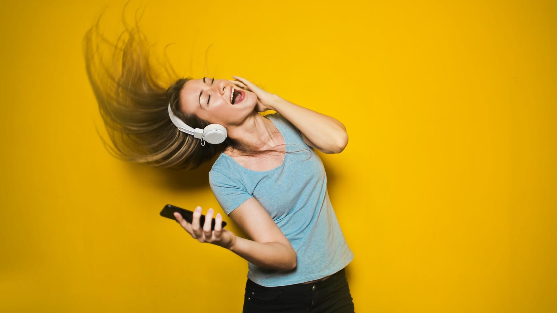 Eine junge Frau mit Kopfhörern und Smartphone tanzt.