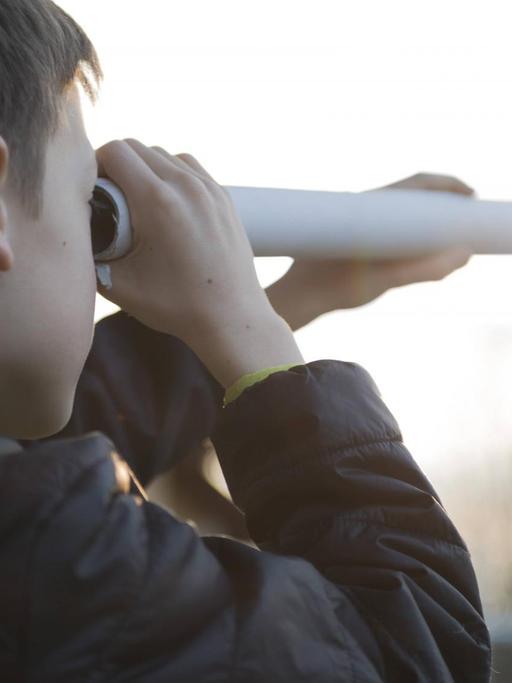 Ein Junge beobachtet durch ein selbstgebautes Teleskop den Himmel.