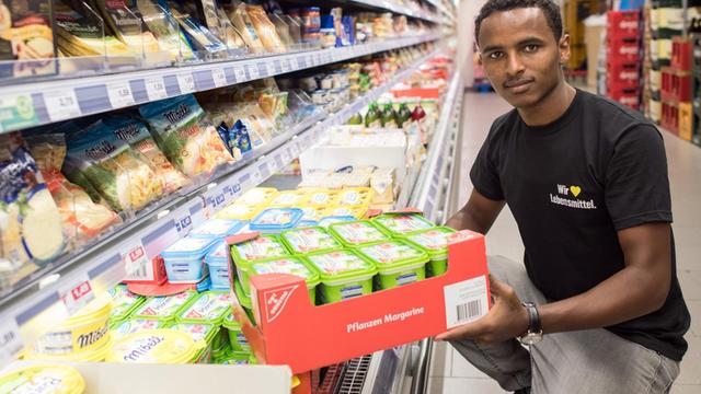 Ein junger Geflüchteter räumt ein Kühl-Regal im Supermarkt ein.