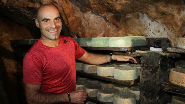 Javier Diaz Bada steht vor einem Regal  mit vom Blauschimmel überzogenem Cabrales Käse in der familieneigenen Höhle