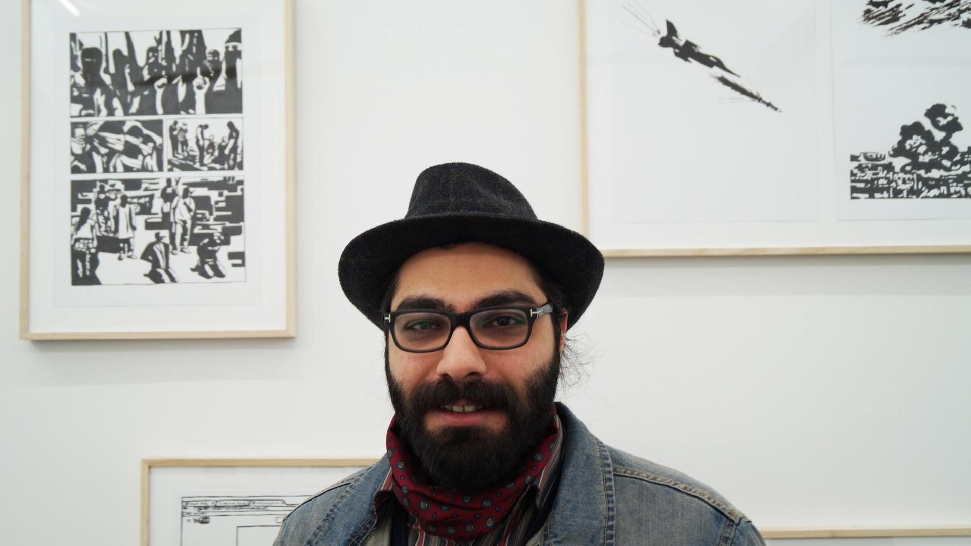 Hamid Sulaiman in seiner Ausstellung "Hamid Sulaiman - Freedom Hospital", Galerie Crone Berlin 9. April - 18. Juni 2016. Der Künstler steht vor den Bildern des Comics.