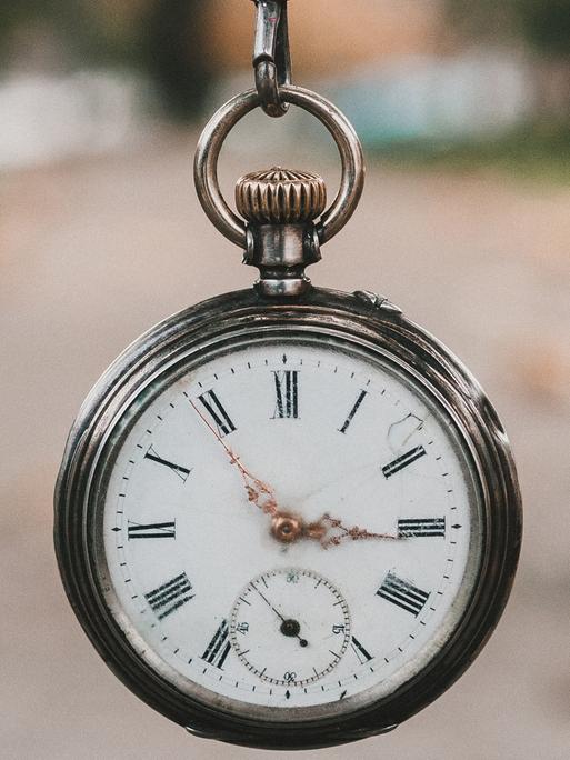 Eine alte Taschenuhr wird an einer Kette vor die Kamera gehalten.