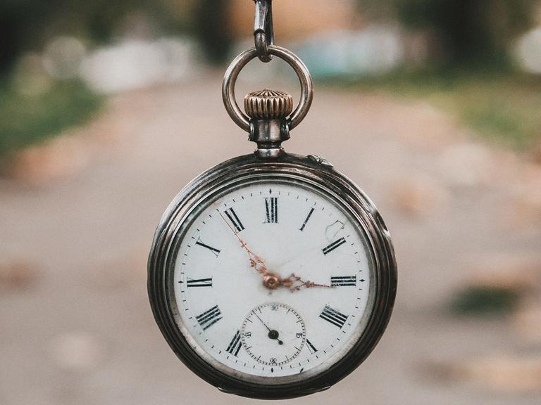 Eine alte Taschenuhr wird an einer Kette vor die Kamera gehalten.
