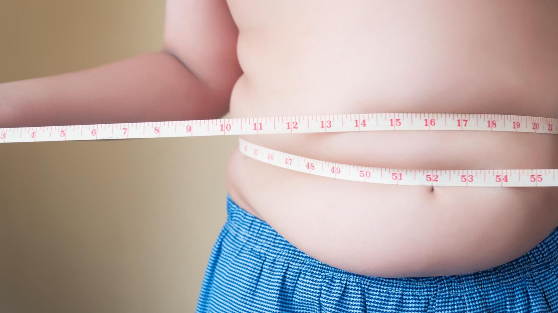 Ein übergewichtiger Junge mißt mit einem Maßband seinen Bauchumfang.