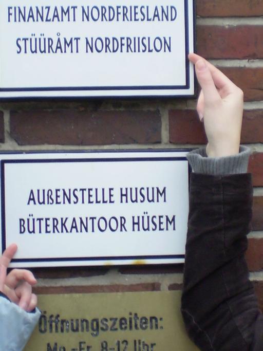 Zwei Friesinnen zeigen stolz das zweisprachige Schild am Finanzamt in Husum