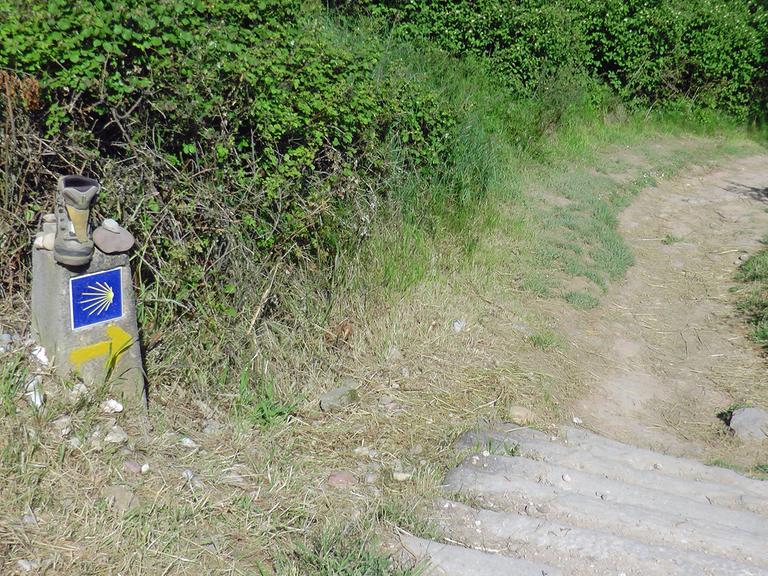 Verlaufen ist fast nicht möglich, so gut ist der Jakobsweg, der Camino, gekennzeichnet: Hier ein Wegstein mit Wanderschuh, Stein und Muschelsymbol in der Nähe des spanischen Ortes Maneru.