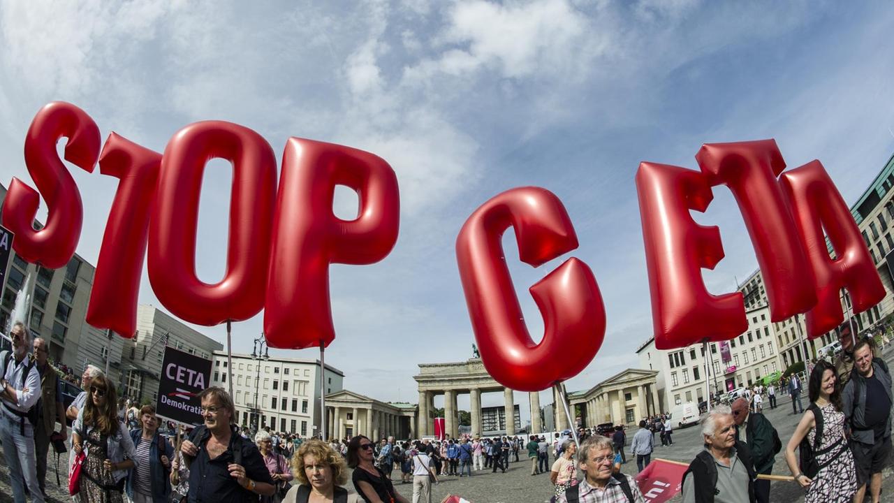 Demonstranten halten rote Buchstaben-Luftballons in den blauen Himme, die die Parole "Stop Ceta" bilden. Im Hintergrund das Brandenburger Tor. 