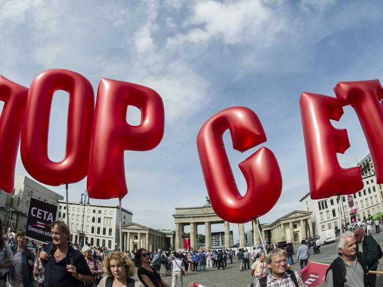 Demonstranten halten rote Buchstaben-Luftballons in den blauen Himmel, die die Parole "Stop Ceta" bilden. Im Hintergrund das Brandenburger Tor.
