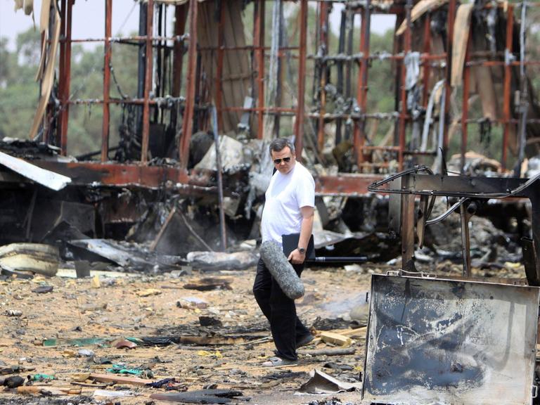 Ein Journalist läuft am 8. Juni 2011 durch eine verwüstete Gegend zehn Kilometer südwestlich von Tripoli in Libyen. Im Hintergrund sind Überreste von ausgebrannten Autos zu erkennen, die durch Luftangriffe von der NATO bombardiert worden sind.