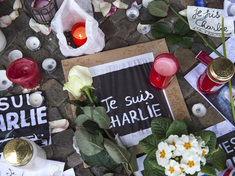 Blumen und Kerzen und Zettel mit der Aufschrift "Je suis Charlie" liegen auf dem Boden.