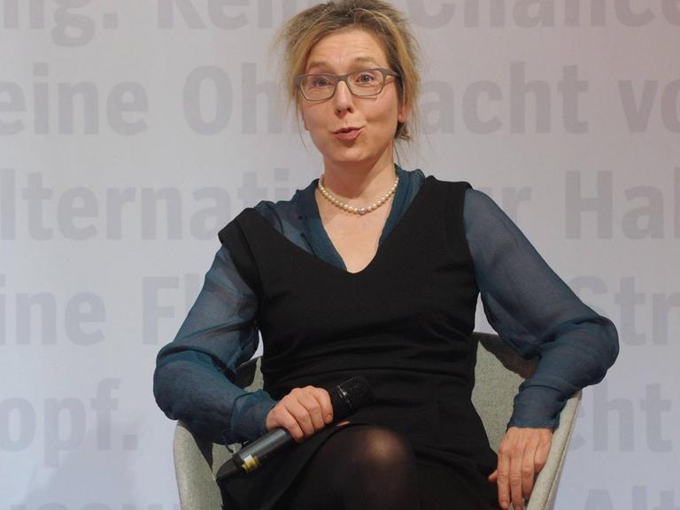 Elke Schmitter sitzt auf einem Sessel auf einem Podium und hält ein Mikrofon in der Hand