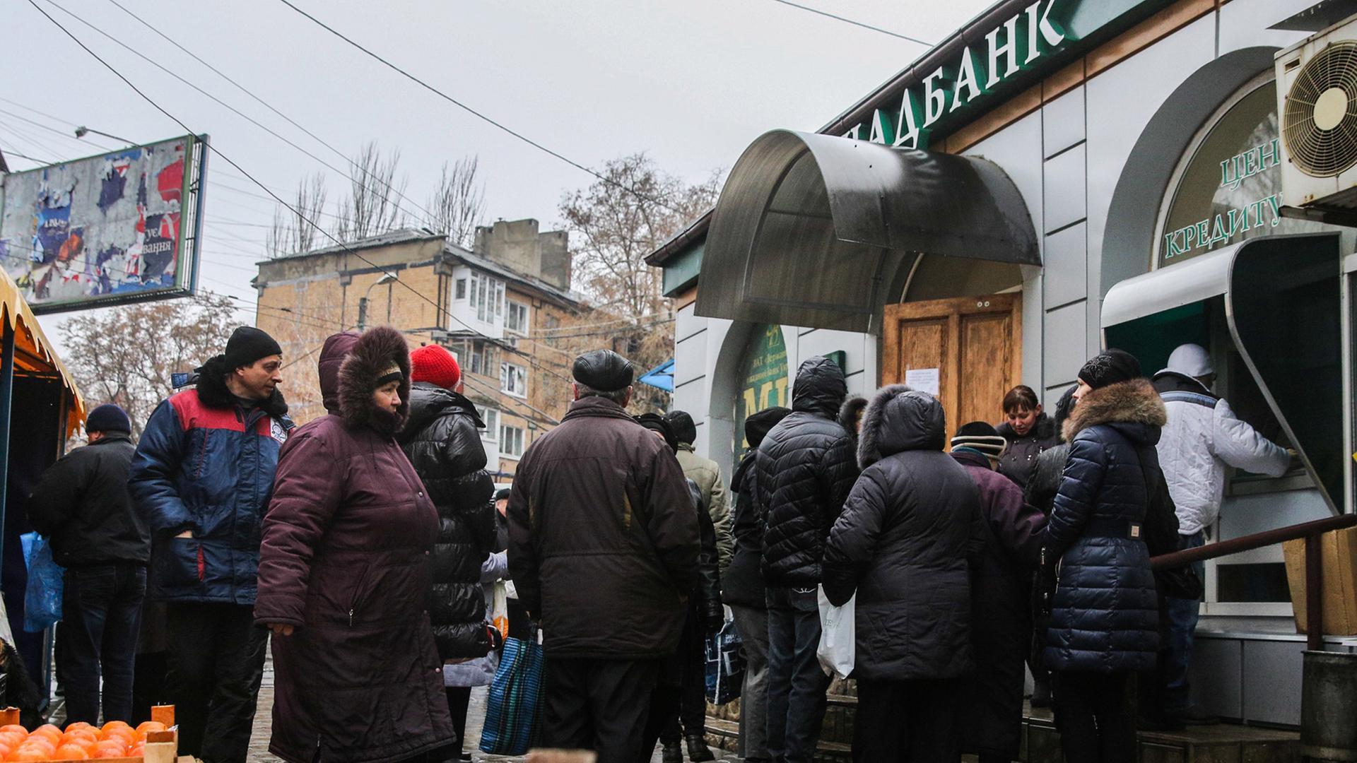 Einwohner von Donetzk warten vor einem Geldautomaten. Im Vordergrund ein Obststand