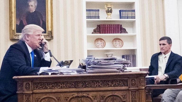 Trump und Flynn sitzen sich an Trumps Schreibtisch gegenüber. 