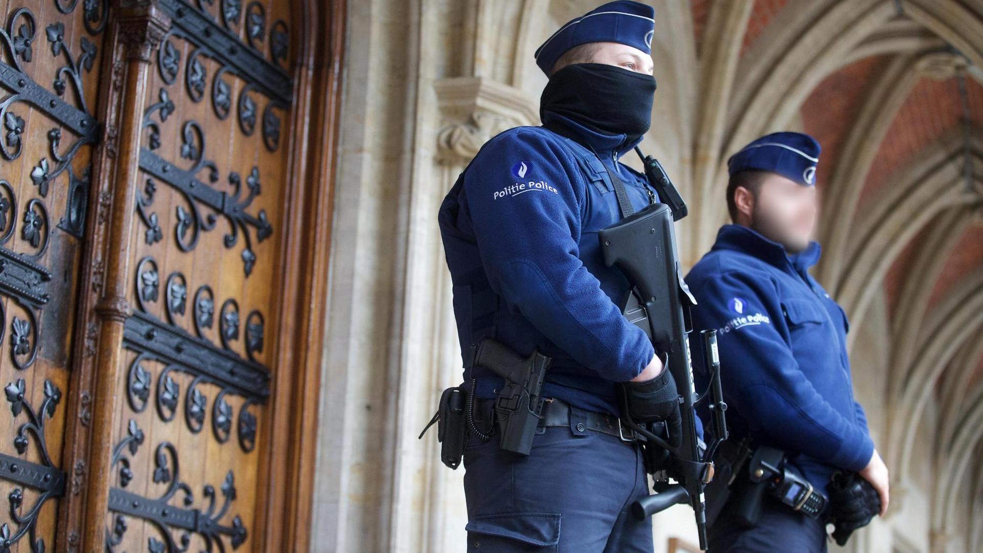 Man sieht zwei Polizisten in blauer Uniform, einer von beiden trägt ein Maschinengewehr.