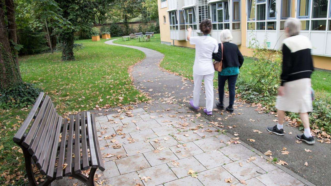 Ein Pflegerin läuft mit zwei pflegebedürftige Damen durch den Garten des beschützenden Bereichs der Münchenstift GmbH.