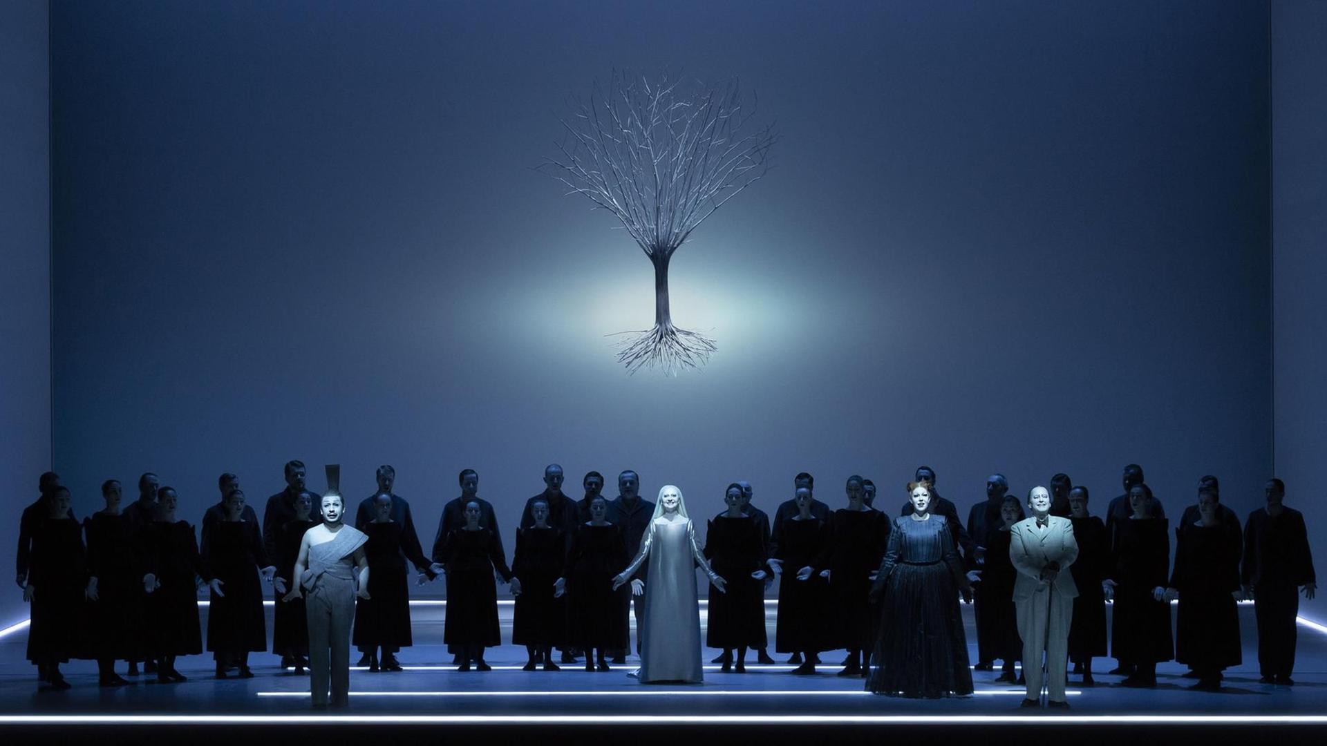 Bläulich schimmernde Szene aus dem Oratorium "Der Messias" in der Inszenierung von Robert Wilson bei der Mozartwoche 2020 in Salzburg: Chor und Solisten stehen auf der Bühne, über ihnen schwebt das Bild eines Baumes mit Wurzelwerk.