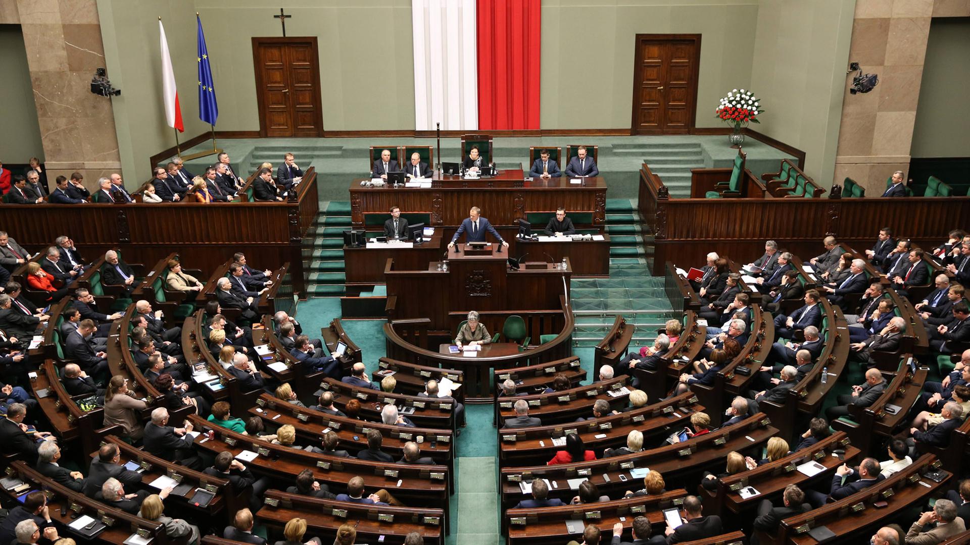 Blick von hinten von der Besuchertribüne auf das vollbesetzte Parlament mit Abgeordneten-Reihen im Halbkreis und das Präsidium unter der polnischen Flagge.