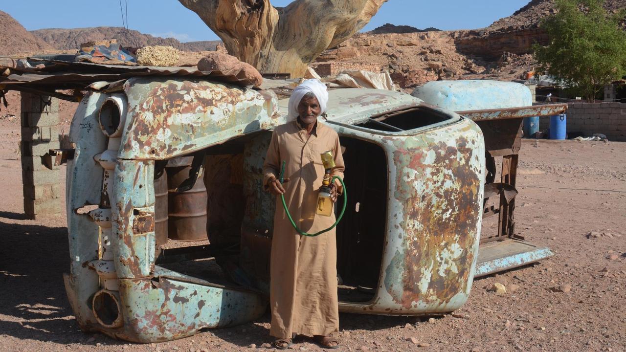 Ibrahim ist der Mann von Umm Yasser und unterstützt sie bei ihrer Arbeit als erste Wanderführerin der Beduinen-Gesellschaft auf dem Sinai. Er steht vor einem umgekippten Schrott-Auto in seinem Dorf.