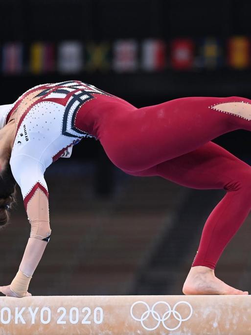 Eine Frau turnt bei den Olympischen Spielen auf einem Schwebebalken, Frauen, sie trägt einen bordeauxrot-weißen Ganzkörperanzug. Es handelt sich um die deutsche Turnerin Pauline Schäfer.