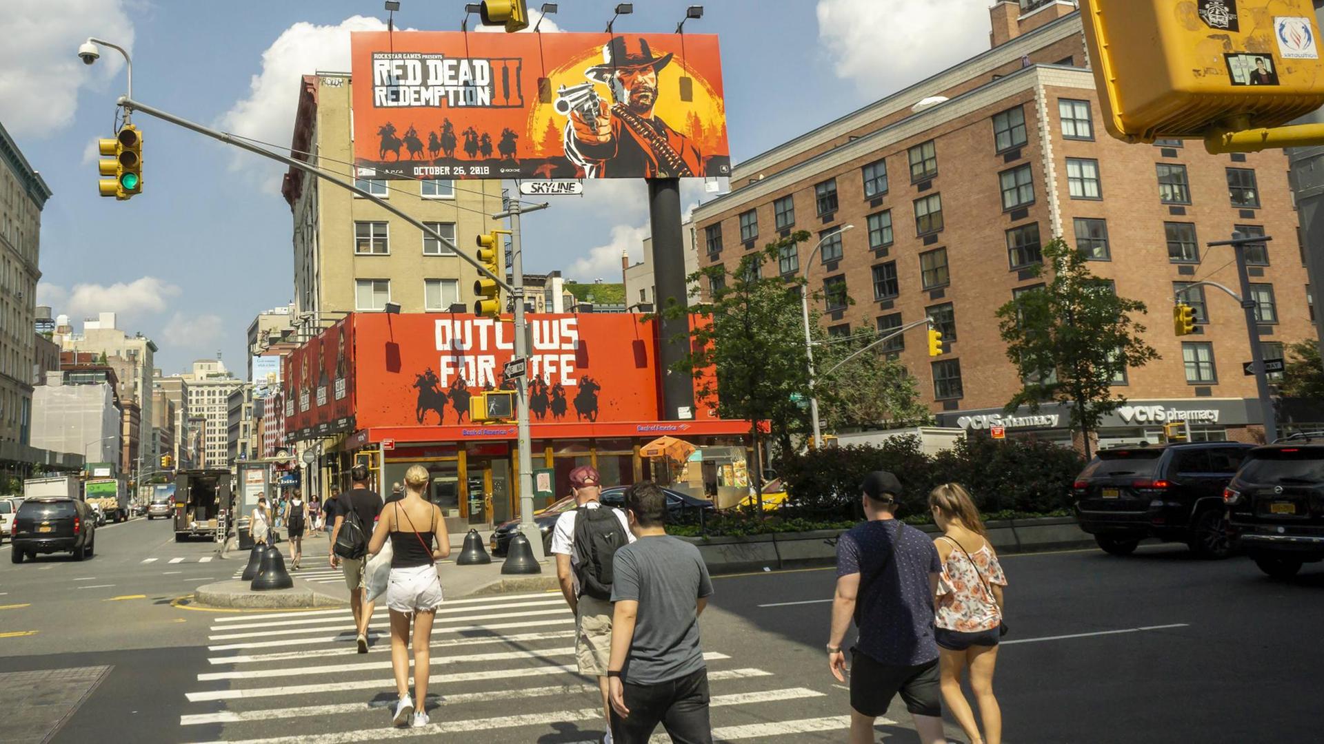 Passanten laufen über einen Zebrastreifen, vor ihnen sind zwei große Plakate zu sehen, auf denen das Computerspiel "Red Dead Redemption 2" beworben wird