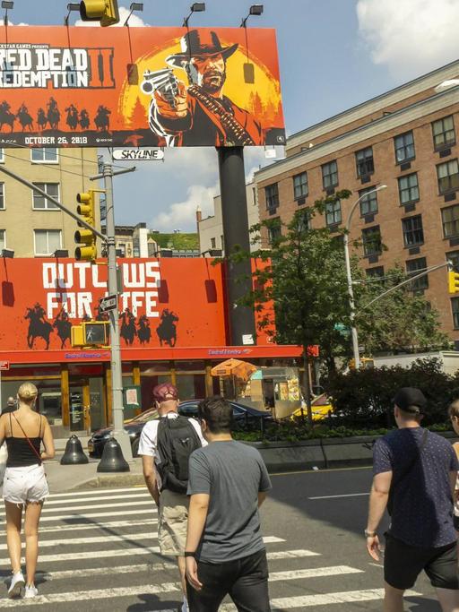 Passanten laufen über einen Zebrastreifen, vor ihnen sind zwei große Plakate zu sehen, auf denen das Computerspiel "Red Dead Redemption 2" beworben wird